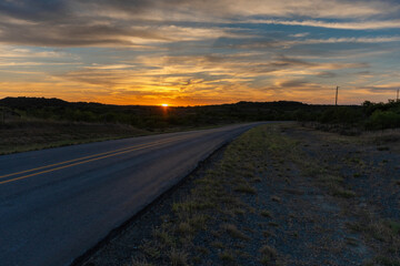 Rural road leading off into distance past sunset in cloudy sky