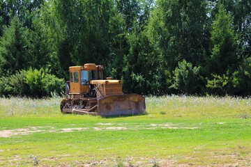 An old bulldozer standing in a field near the forest. Background. Landscape.