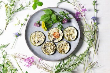 Baked rings of squash with herbs and cheese on plate decorated with forest flowers