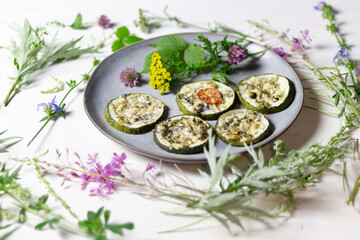 Baked rings of squash with herbs and cheese on plate decorated with forest flowers
