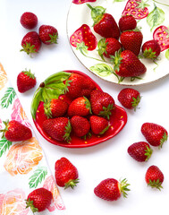 Two plates of ripe strawberry on white background. Red berry concept with berries dish and kitchen towel with roses.