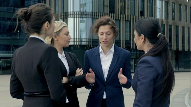 Female confident boss giving instructions to subordinates women workers after the business meeting, standing outdoor the modern building office center 