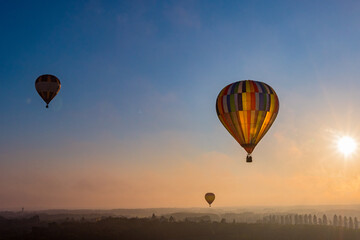 Flug von drei Heißluftballons über hügeliger Landschaft morgens bei Sonnenaufgang im Gegenlicht