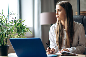 Home schooling. Beautiful caucasian female student is studying at home online using a laptop