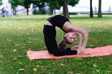 Fototapeta premium A girl of school age doing gymnastics in a park on the grass.