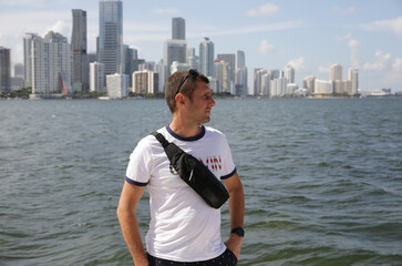 active young man with fashionable belt bag on the background of the city and water of the river or sea