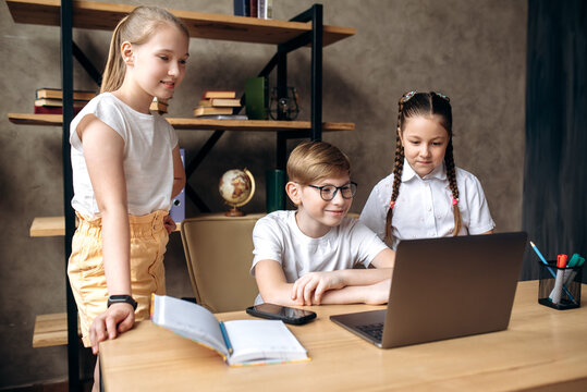Learning in small groups. Three caucasian school children, one boy and two girls are sitting in a classroom and watching a school lesson by online conference