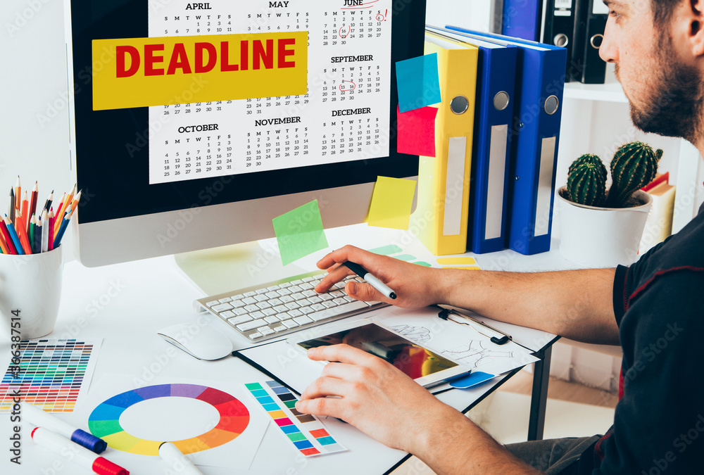 Fototapete young handsome graphic designer using graphics tablet looking on calendar with deadline date