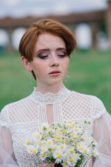 Pretty young caucasian redhead girl in a garden and outside with her wedding bouquet. Beautiful redhead bride.