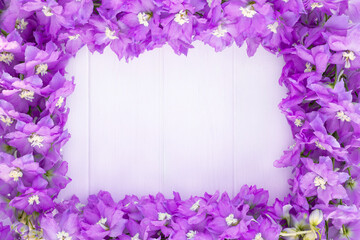 Frame made of lilac delphinium flowers on a white plank background. Top view. Copy space.
