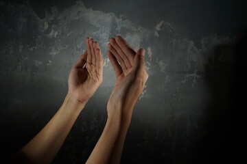 Fototapeta na wymiar Hand praying in front of grey grunge wall texture with focused lighting.
