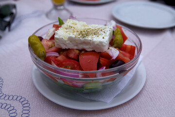 Traditional Greek salad of fresh vegetables with feta cheese, sprinkled with spices, in a transparent bowl 