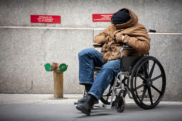 A disabled homeless veteran sits in a wheelchair on a sidewalk in New York City.