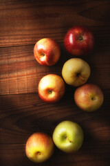 High angle shot of a group of  fresh picked apples on a rustic wood table. Fuji, Gala, Granny Smith, Braeburn, Golden Delicious with warm side light.