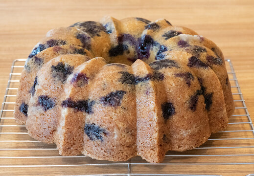 Home baked blueberry bundt cake fresh from the bundt pan is cooling on a metal wire rack on a wooden board.