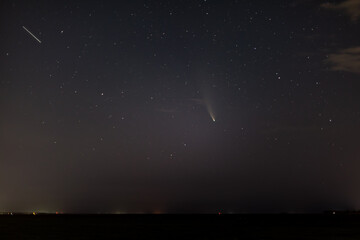 Comet NEOWISE, a satellite in the dark starry sky with clouds above the horizon at night. Horizontal orientation. 