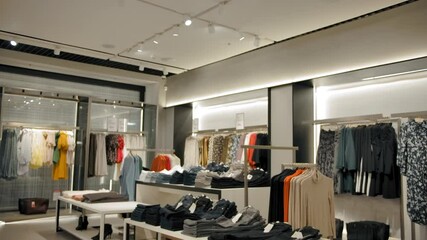Wide vertical panning shot indoor of clothing store with modern fashionable cloth hangers and shoes. Dresses sweaters jeans, trousers tops and other clothes. - Powered by Adobe