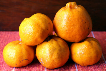 Five tangerines are on a red tablecloth.