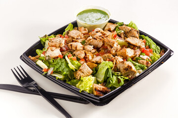 Grilled chicken salad with dressing in a carry-out container