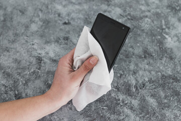 the new normal after covid-19,  hand cleaning smartphone with disinfectant wipe to flatten the curve and prevent viruses and bacteria