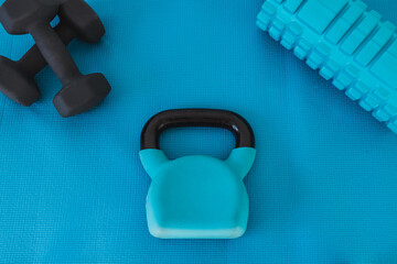 home gym concept, blue yoga mat with kettlebell foam roller and dumbbell shot at shallow depth of field from low perspective.