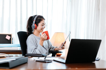 woman working on laptop and hold cup of coffee while sitting at working place.