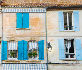 Colorful blue shutters by arched windows with flowers in boxes old brick building in france