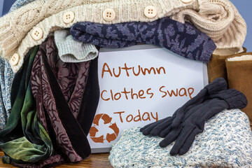 Preloved clothes in a box marked with board sign Autumn clothes swap and recycle textiles symbol,...