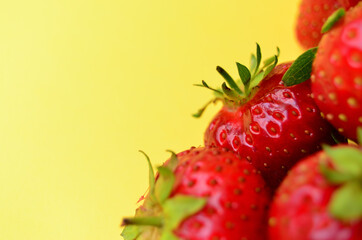 a bunch of ripe fresh red strawberry berries lying in the bottom right corner on a yellow background with a copy space