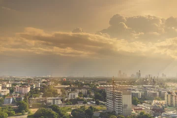 Foto op Canvas View of expanding city, changing environment. In the evening, the sun shines through cloudy sky and rain from the tower © Thanawang3rd