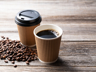 A paper cup of coffee and coffee beans on an old wooden background