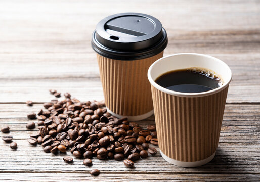 A paper cup of coffee and coffee beans on an old wooden background
