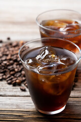 Cold coffee in a glass with coffee beans behind it.