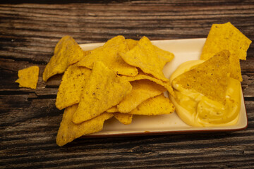 Corn chips with cheese sauce on a wooden background. Close up.