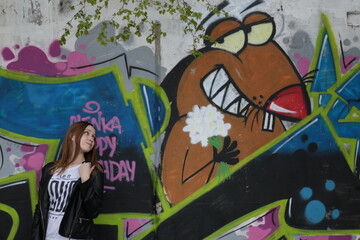 Beautiful young girl in black leather jacket against graffiti wall