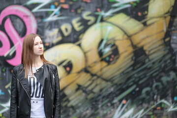Beautiful young girl in black leather jacket against graffiti wall