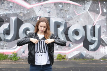 Fototapeta na wymiar Beautiful young girl in black leather jacket against graffiti wall