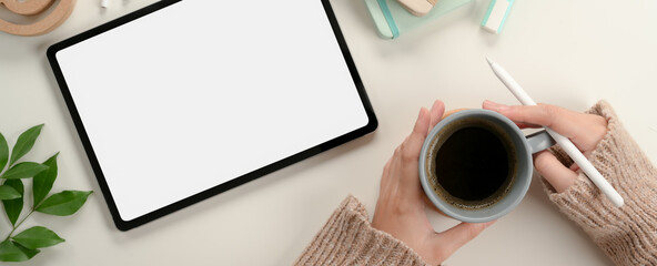 Female student hands holding coffee mug while working with mock up tablet on study table