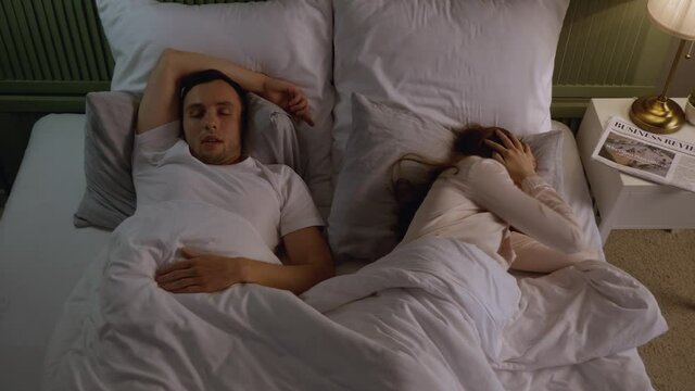 Young irritated woman in bed with snoring husband