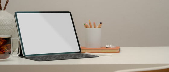 Blank screen tablet with keyboard on white table with stationery, coffee cup and copy space