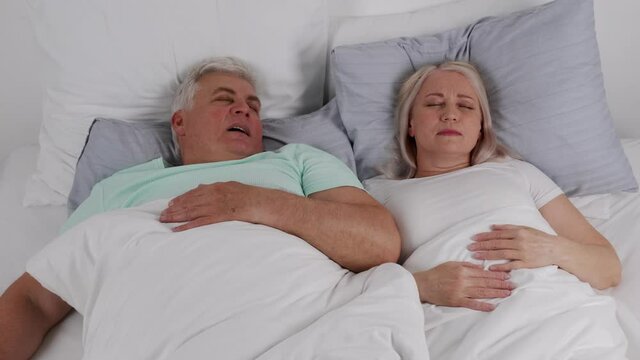Mature woman pinching nose of snoring husband in bed