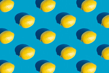 Pattern with ripe yellow lemon with a hard shadow on blue background. Minimum summer background. Concept of healthy eating.