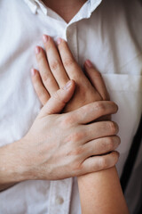 male hand presses a female hand to his chest. a man in a white shirt gently pressed a woman's hand to his chest. 