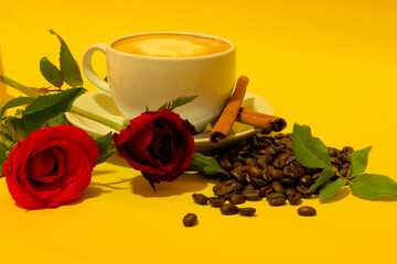 Cup of freshly ground and brewed coffee with coffee beans, cinnamon sticks and red roses on a golden yellow background
