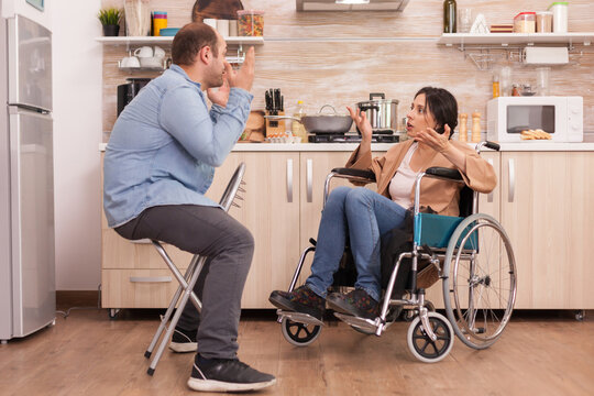 Disabled wife in wheelchair shouting at husband in kitchen. Disabled paralyzed handicapped woman with walking disability integrating after an accident.