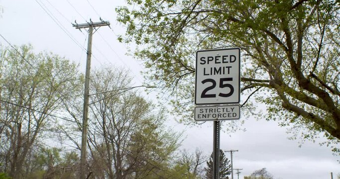 Speed limit sign with power lines and trees above it in a Low Angle and a car passing