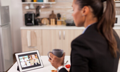 Businesswoman in the morning having an online conference call while eating breakfast in the kitchen.