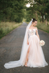 Gorgeous bride in elegant wedding dress stand in linden alley with bouquet and posing to photographer