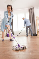 Wife housekeeping using mop and husband vacuum cleaner.
