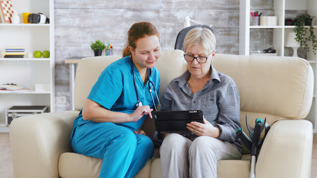Female nuse helping senior elderly retired woman how to use her tablet computer in nursing home